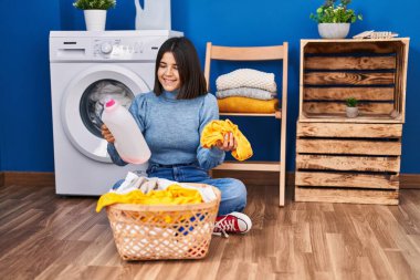 Çamaşır odasında çamaşır deterjanı şişesini tutan güzel İspanyol kadın.