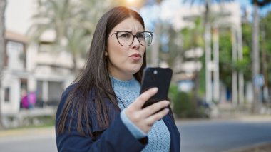 Genç İspanyol kadın akıllı telefon kullanıyor. Park 'a üzgün bakıyor.