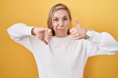Beyaz süveter giyen beyaz bir kadın sarı arka planda baş parmak hareketi yapıyor. Anlaşmazlık ve uzlaşma ifadesi. çılgın çatışma 