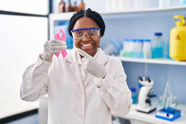 Afrika kökenli Amerikalı bir kadın, elinde pembe kurdeleyle laboratuvarda çalışıyor. 