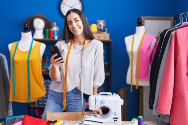 Elbise fabrikasında akıllı telefon kullanan, kendine güvenen, güzel İspanyol bir terzi.