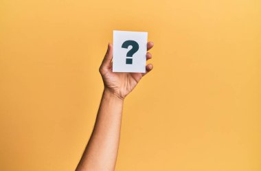 Hand of caucasian man holding paper with question mark over isolated yellow background