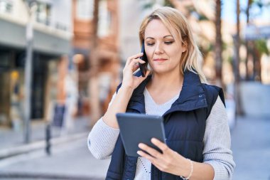 Genç sarışın kadın akıllı telefondan konuşuyor. Sokakta dokunmatik ped kullanıyor.