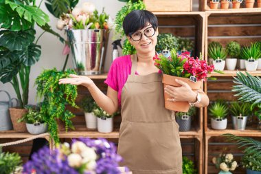 Çiçekçi dükkanında çalışan kısa saçlı genç Asyalı kadın başarıyı mutlu bir gülümsemeyle ve el kaldırarak kutluyor. 