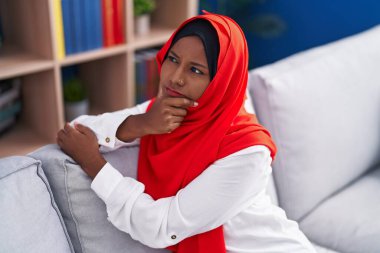 Young beautiful woman sitting on sofa with serious expression at home