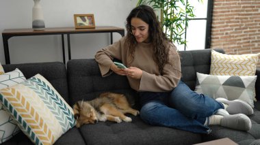 Köpekli genç İspanyol kadın akıllı telefonla evde uyuyan köpeğe fotoğraf çekiyor.