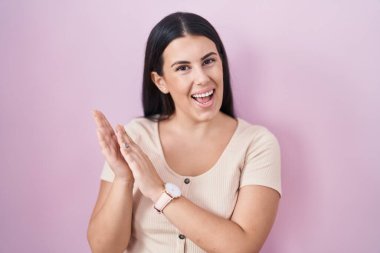 Pembe arka planda duran genç İspanyol kadın alkışlıyor ve alkışlıyor mutlu ve neşeli, birlikte gülümseyen gururlu eller 