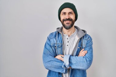Yün şapkalı, mutlu yüzlü, kolları çapraz gülümseyen ve kameraya bakan İspanyol dövmeli genç adam. pozitif kişi. 