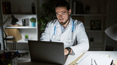 Genç İspanyol doktor klinikte çalışırken dizüstü bilgisayar kullanıyor.