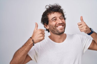 Young hispanic man smiling confident doing ok sign with thumbs up over isolated white background