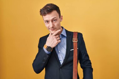 Sarı arka planda beyaz iş adamı kameraya kollarını kavuşturup gülümseyen ve çenesini kaldıran kendinden emin bir şekilde bakıyor. Olumlu düşünmek. 