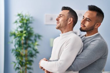 Two men couple hugging each other standing at home