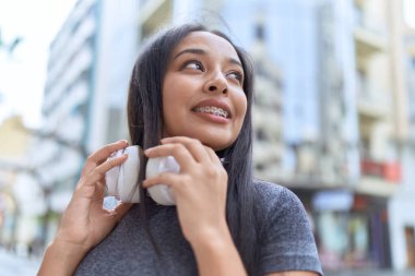 Genç Arap kadın sokakta kulaklık takarak gülümsüyor.