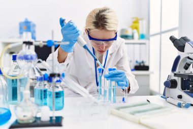 Laboratuvarda test tüpüne sıvı döken genç sarışın bilim kadını.
