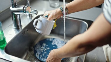 Orta yaşlı İspanyol kadın mutfakta tabak yıkıyor.