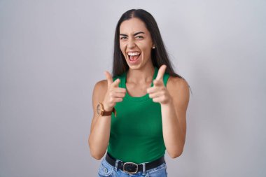 İzole edilmiş arka planda duran genç bir kadın mutlu ve komik yüzlü parmaklarını kameraya doğrultuyor. iyi enerji ve titreşimler. 