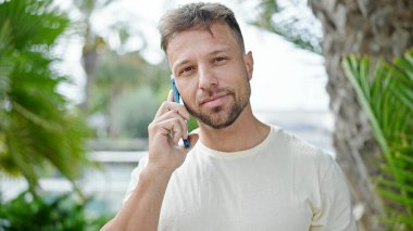 Parkta yürürken ciddi bir ifadeyle akıllı telefondan konuşan genç adam.