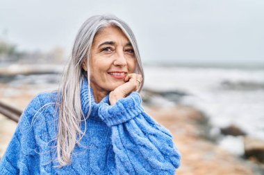 Orta yaşlı, kır saçlı, gülümseyen, kendine güvenen bir kadın.