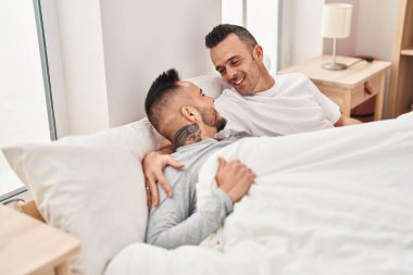 Two men couple lying on bed hugging each other at bedroom