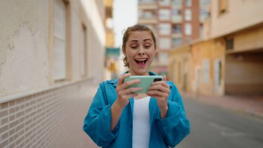 Sokakta akıllı telefondan video seyreden kendine güvenen genç bir kadın.