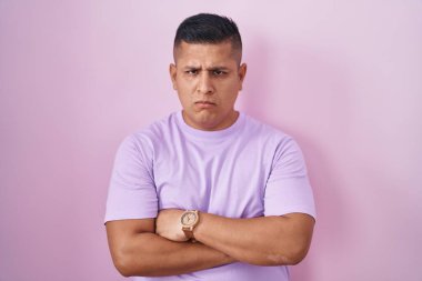 Young hispanic man standing over pink background skeptic and nervous, disapproving expression on face with crossed arms. negative person. 