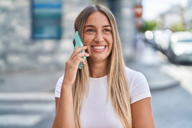 Genç, güzel, İspanyol bir kadın gülümsüyor ve caddede akıllı telefondan konuşuyor.