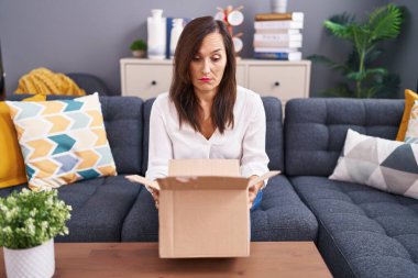 Orta yaşlı esmer kadın, karton kutuyu şüpheci ve gergin bir şekilde açıyor, sorun yüzünden kaşlarını çatıyor. negatif kişi. 