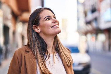 Young beautiful hispanic woman smiling confident looking to the sky at street