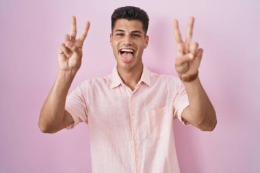 Pembe arka planda dikilmiş, ağzı açık gülümseyen genç bir İspanyol zafer işareti yapıyor. İki numara.. 