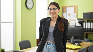 Genç, güzel, İspanyol bir iş kadını. Ofiste kendinden emin bir şekilde gülümsüyor.