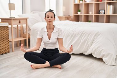 Young caucasian woman doing yoga exercise sitting on floor at bedroom
