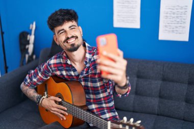 Genç İspanyol ressam, müzik stüdyosunda klasik gitar çalarak akıllı telefondan selfie çekiyor.