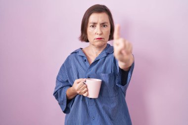 Orta yaşlı İspanyol bir kadın kahve içerken parmağını kaldırmış ve kızgın bir ifade takınıyor. 