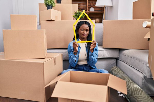 Африканская женщина с косичками сидит на полу в новом доме, держа правителя скептически и нервно, хмурясь расстроен из-за проблемы. отрицательный человек. 