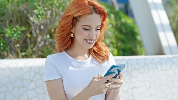 Young redhead woman using smartphone smiling at park