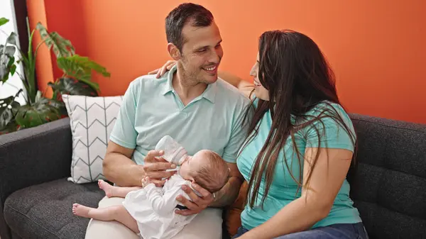 三个喂养婴儿的家庭坐在家里的沙发上 — 图库照片