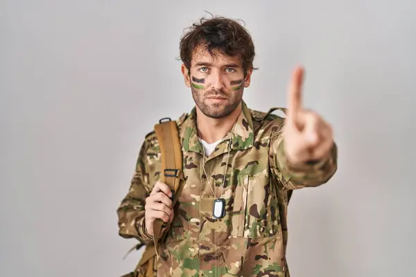 Hispanic young man wearing camouflage army uniform pointing with finger up and angry expression, showing no gesture
