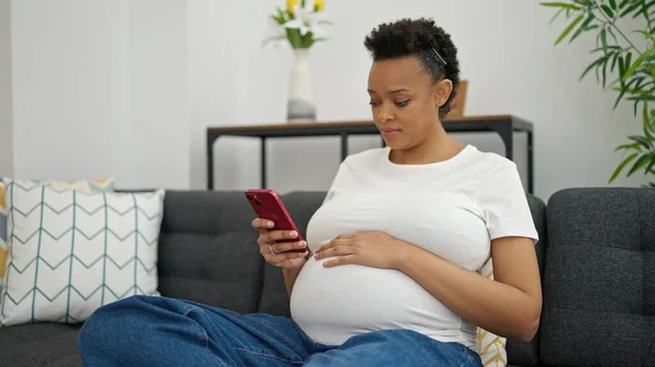 Junge Schwangere Sitzt Mit Smartphone Hause Auf Sofa — Stockfoto