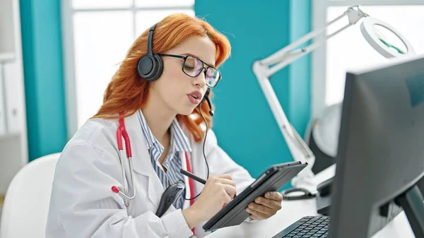 stock image Young redhead woman doctor on video call writing on touchpad at clinic