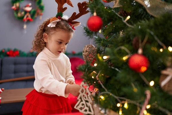 自宅でクリスマスツリーを飾るトナカイ耳を着用する愛らしいブロンドの少女 — ストック写真