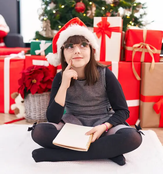 Adorable Hispanic Girl Sitting Floor Christmas Tree Doubt Expression Home — Stock Photo, Image