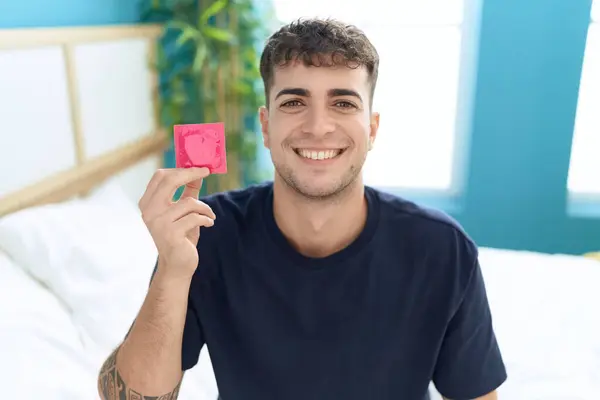 Young Hispanic Man Sitting Bed Holding Condom Looking Positive Happy — Stock Photo, Image