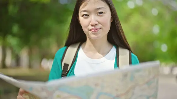 Young chinese woman tourist wearing backpack looking at city map at park