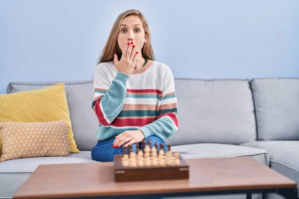 Mladá Blondýnka Hrající Šachy Sedící Pohovce Zakrývající Ústa Rukou Šokovaná — Stock fotografie