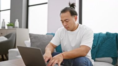 Kanepede dizüstü bilgisayar kullanan yakışıklı genç bir adam. Belli ki evde şiddetli karın ağrısı çekiyor.