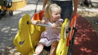 Kafkasyalı anne ve istekli kız tahterevallide oturuyor, parkta ciddi ciddi oyun oynuyor, dışarıda ailecek vakit geçiriyorlar.