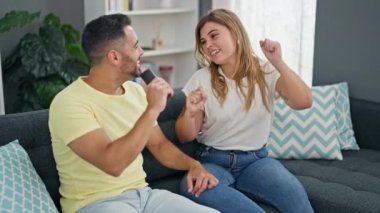 Kanepede oturan erkek ve kadın çift evlerinde mikrofon olarak uzaktan kumandayla şarkı söylüyorlar.