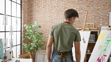 Kendine güvenen İspanyol genç, gelişmekte olan bir sanat meraklısı, kollarıyla çapraz gülümseyen tamamen dalmış yaratıcı bir stüdyo sınıfında, öğrenme ve resim yapma büyüsünü ateşleyen ve zevk alan