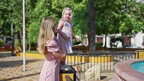 自信に満ちた母親 娘の周りに包まれた腕 日光浴公園にいる笑顔 ポジティブさと幸せを放射する — ストック動画
