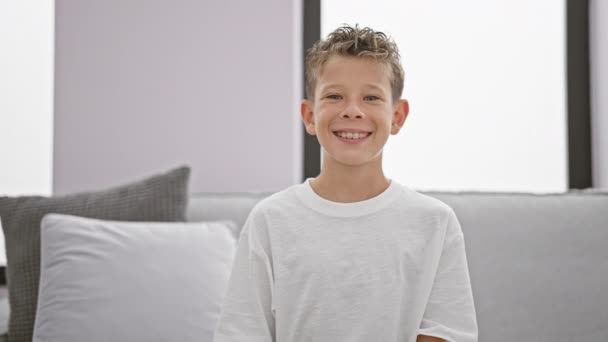 可爱的金发碧眼的男孩 充满自信和欢乐 带着愉快的笑容 舒服地躺在家里的沙发上 — 图库视频影像